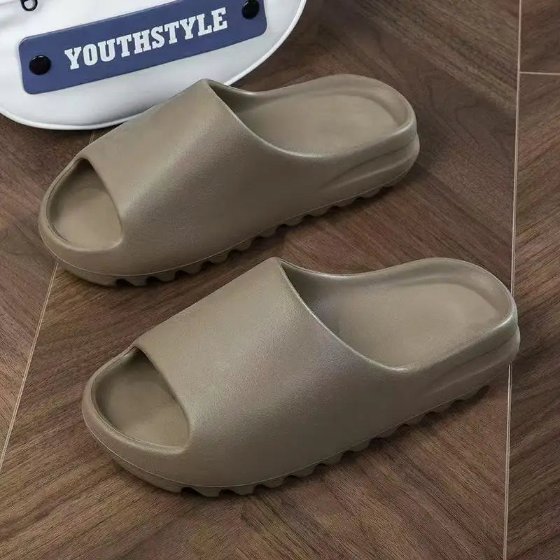 A pair of beige cloud thick-soled EVA slides for men and women resting on a wooden surface.