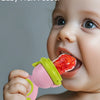 A baby is shown using a pink and lime green rotating silicone fruit feeder to feed a piece of fruit.