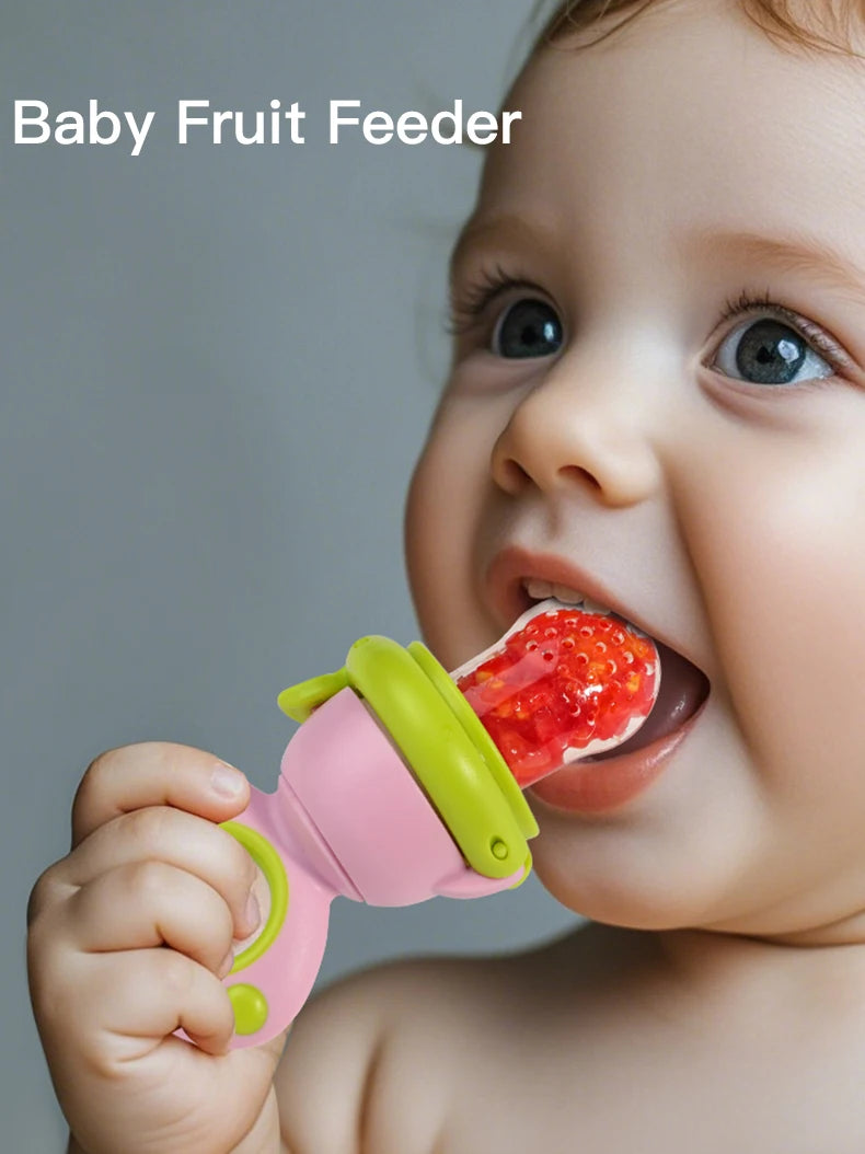 A baby is shown using a pink and lime green rotating silicone fruit feeder to feed a piece of fruit.