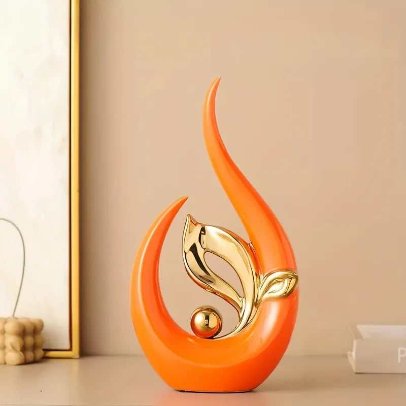 An orange ceramic sculpture shaped like a stylized leaf or flame, featuring gold accents.