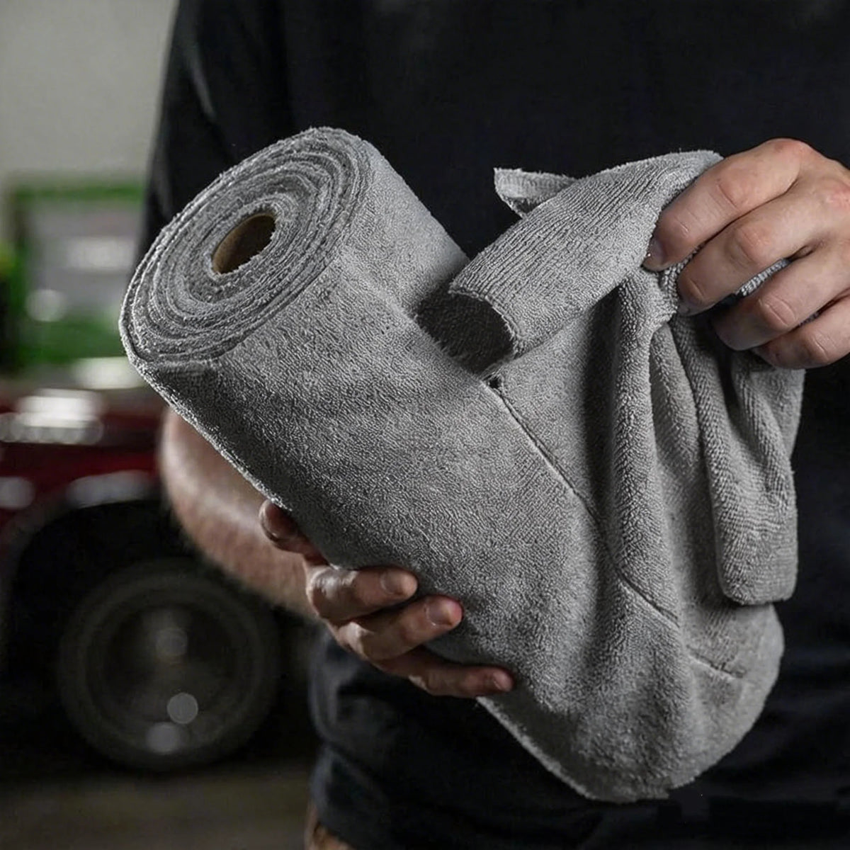 A hand holds a roll of gray microfiber cleaning cloths.
