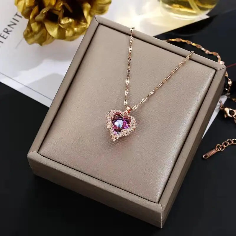 Collier délicat en or avec pendentif de cœur en cristal rose, présenté dans une boîte rectangulaire.
