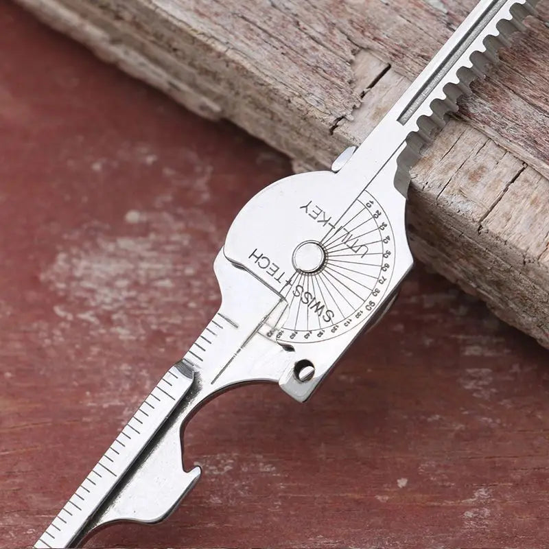 Silver multi-tool keychain with a serrated blade and a marked scale on a wooden surface.