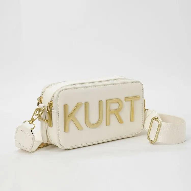 Eine cremefarbene Leder-Tasche mit dem Namen KURT in goldener Beschriftung.