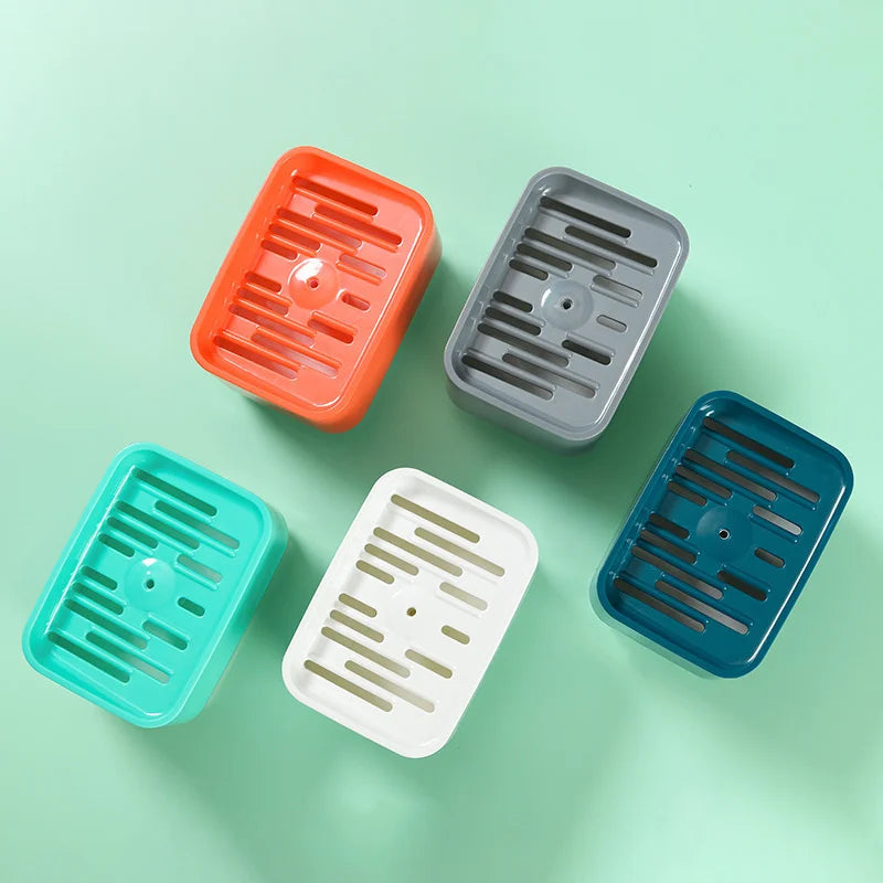 Four silicone kitchen soap dispensers in orange, gray, teal, and blue with sponge holders arranged on a light green surface.