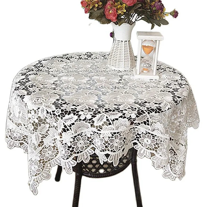 White lace tablecloth with embroidered rose design set on a table.
