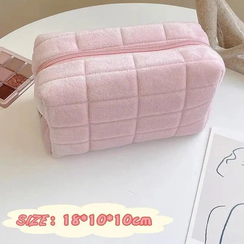 A soft pink quilted portable makeup bag with a zipper is displayed on a white surface.