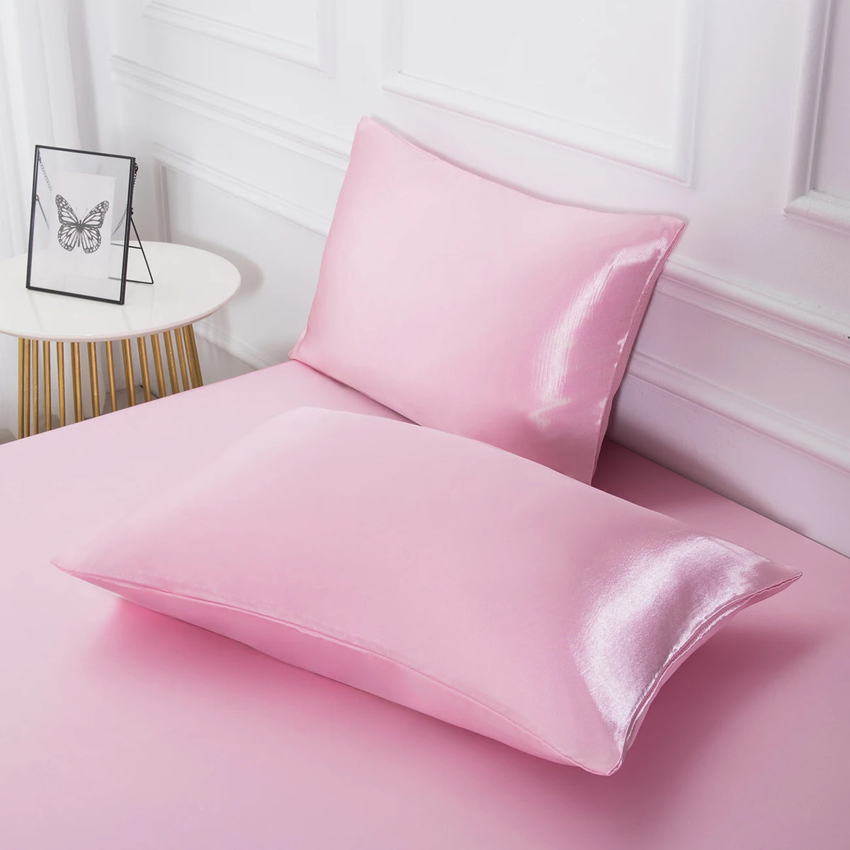 Ein rosa Satinkissen wird auf einer rosa Fläche neben einer weißen Wandleiste präsentiert.