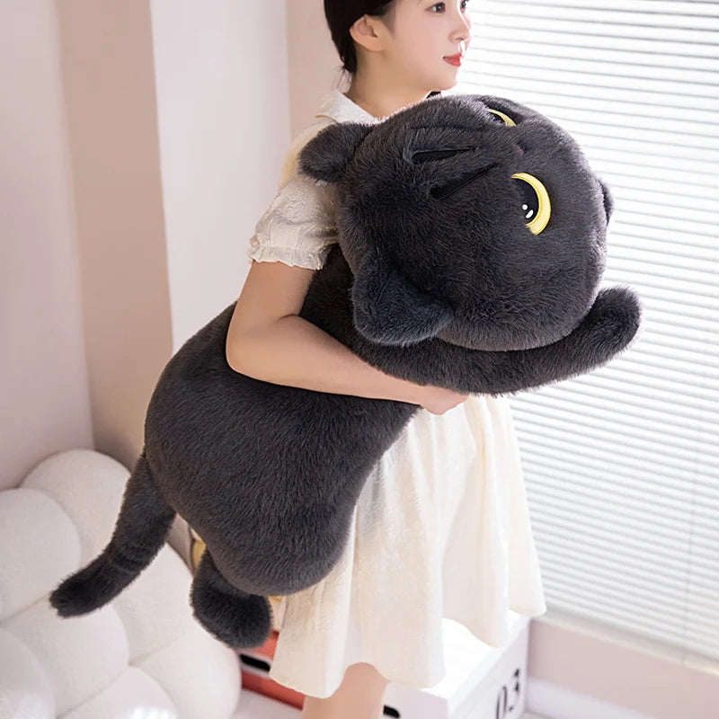 A woman is holding a soft black cat plush toy, which resembles a cuddly companion pillow.