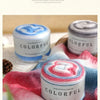 A close-up of Colorful Long distance cake yarn in various shades resting on a pink and blue knitted fabric.