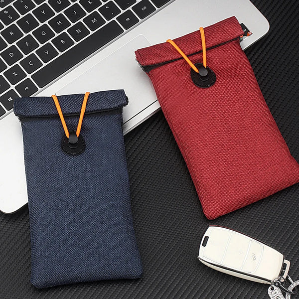 Bolsa de bloqueo Faraday azul oscuro para llaves de coche y teléfonos, sobre una superficie negra.
