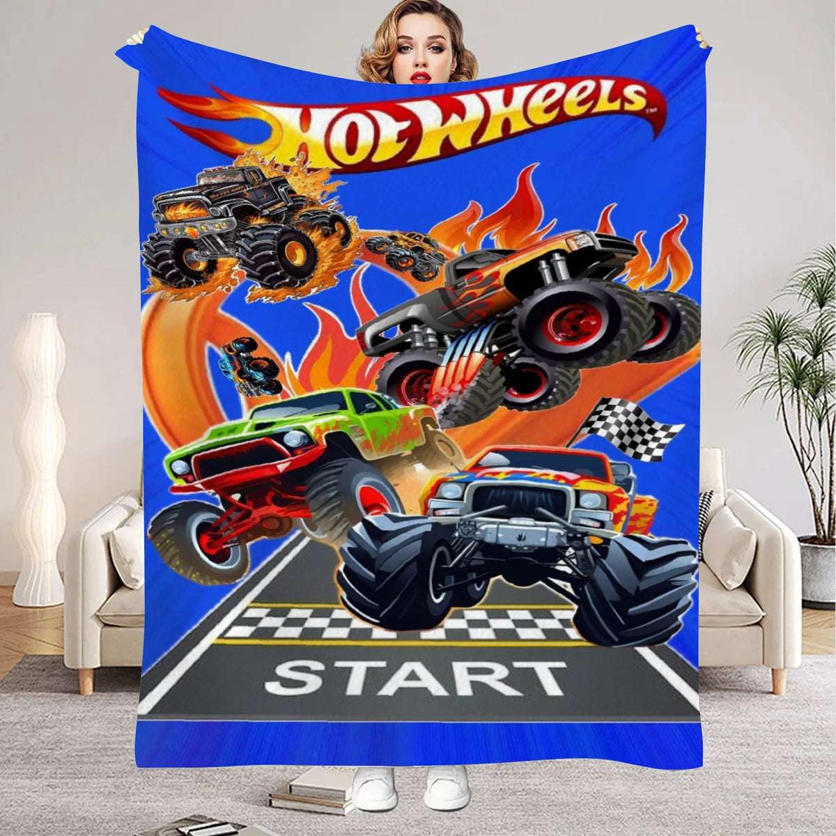 A colorful flannel throw blanket featuring a cartoon design of various monster trucks and the Hot Wheels logo.