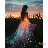 A woman stands silhouetted against a sunset, with sparkling light trails flowing from her dress.