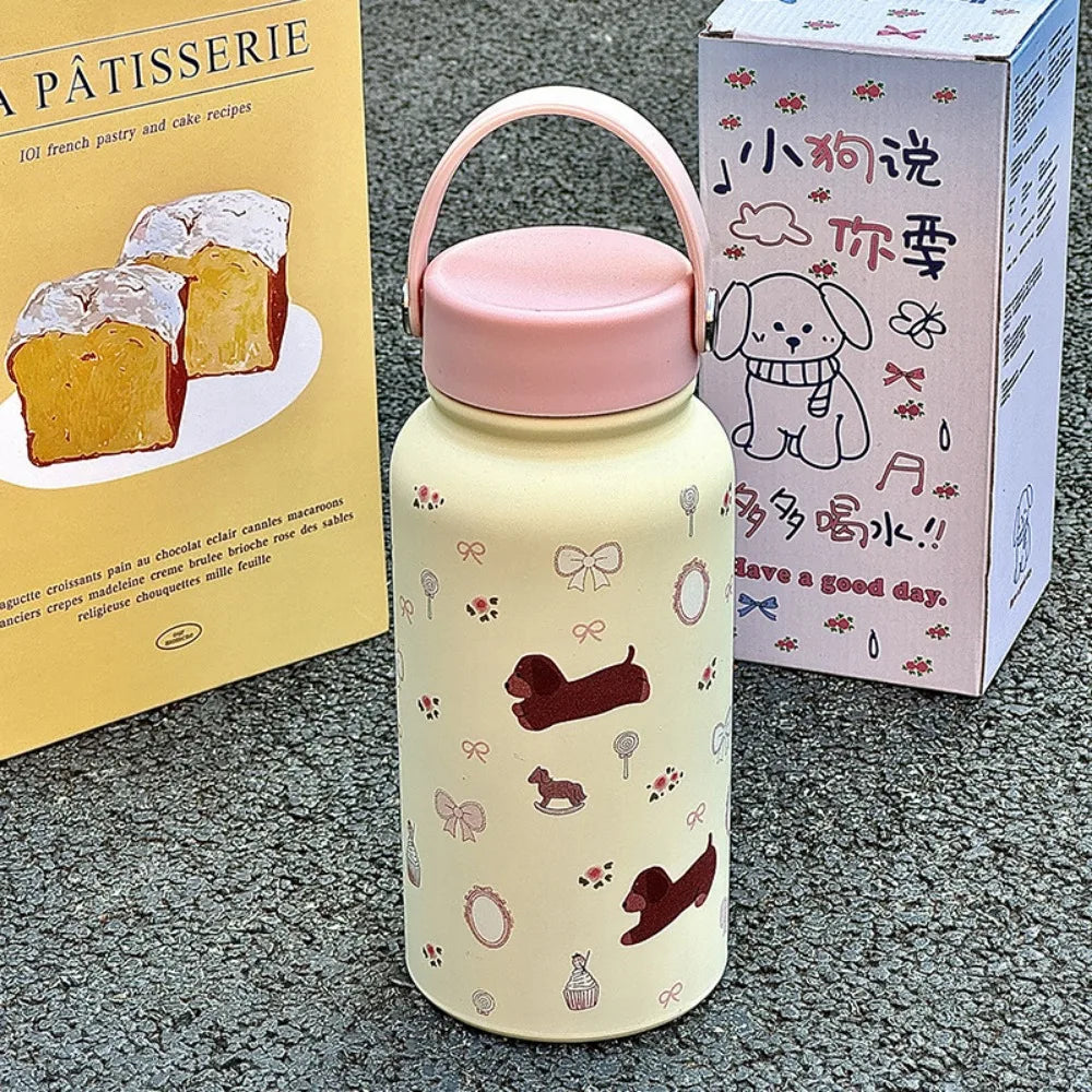 A light yellow insulated tumbler with a pink lid and decorative motifs sits next to a cookbook.