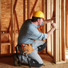 A man wearing a yellow hard hat and work clothes is installing wooden framing inside a structure.