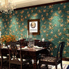 A richly decorated dining room featuring dark wood furniture and a teal floral wallpaper backdrop.