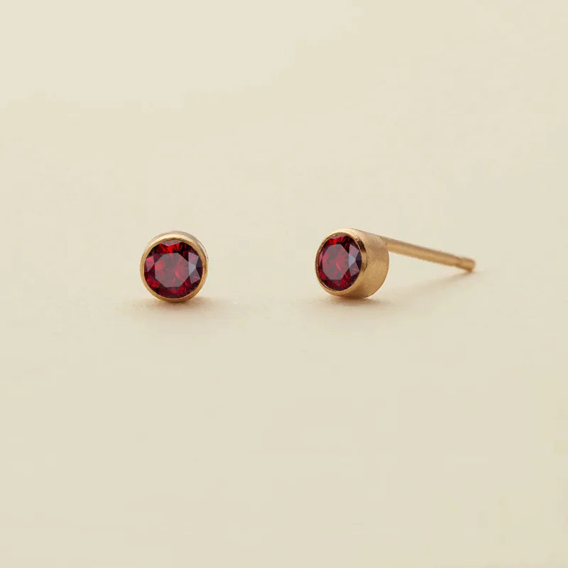 Boucles d'oreilles à clous de naissance minimalistes ton or, avec un joyau rouge profond.
