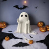 A white ghost resin statue with outstretched hands sits on a white fluffy surface against a dark background decorated with ba