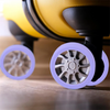 A close-up view of four purple silicone wheel protectors on a yellow suitcase caster wheel.