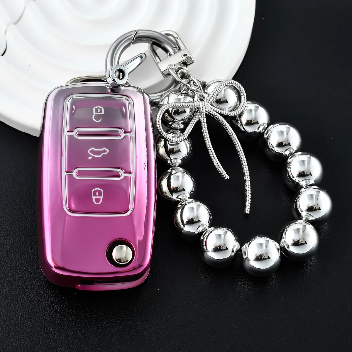 A pink soft TPU car key cover with a metal keyring and chain attached to a silver charm bracelet.