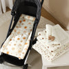 A white padded stroller seat cushion with a sunburst pattern is displayed next to a stack of similar cushions.