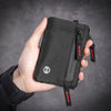 A hand holds a black RFID-blocking travel wallet with a red carabiner clip against a dark gray background.