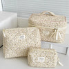 A set of vintage floral quilted cosmetic bags in cream and beige fabric displayed on a white shelf.