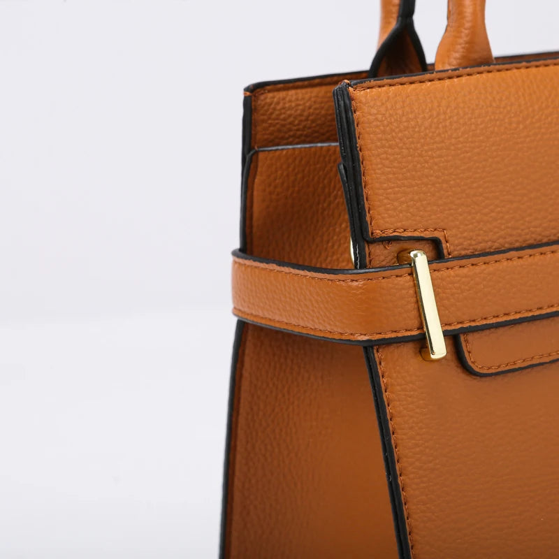 A close-up of a tan leather handbag with black trim and gold hardware.