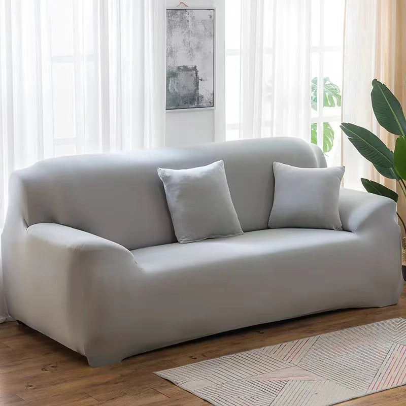 A light gray elastic stretch sofa cover for a modern couch placed in a bright room.