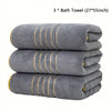 Three gray bath towels with gold accents stacked neatly.