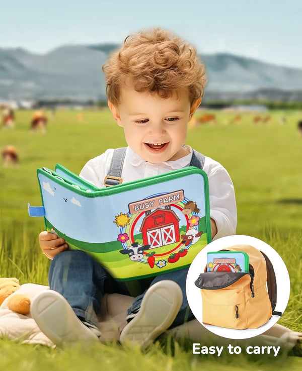 A toddler is holding a colorful felt quiet book outdoors in a grassy field.