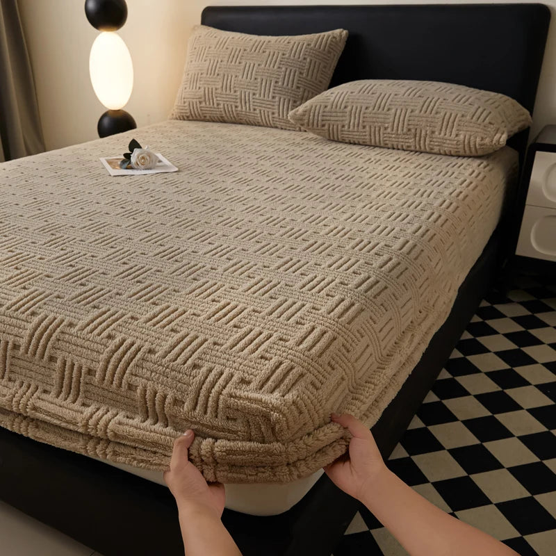 A hand is adjusting the elastic edge of a beige woven mattress cover on a dark bed.