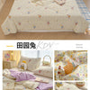 A light yellow and white quilt featuring a playful cartoon print of animals and flowers on a bed.