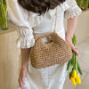 A woman wearing a white dress holds a woven straw chain crossbody handbag.