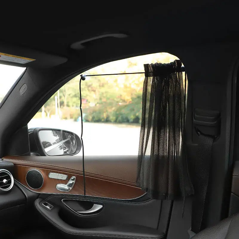A black sunshade is installed in a car window using suction cups, visible inside the vehicle.