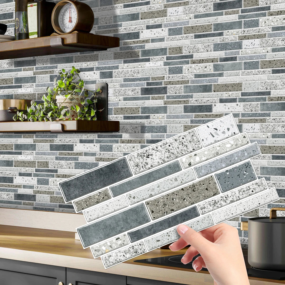 A hand is placing rectangular peel-and-stick tile stickers onto a gray and white subway tile backsplash.