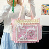 A pink transparent shoulder bag with white lace trim and a pink floral design is held by a person.