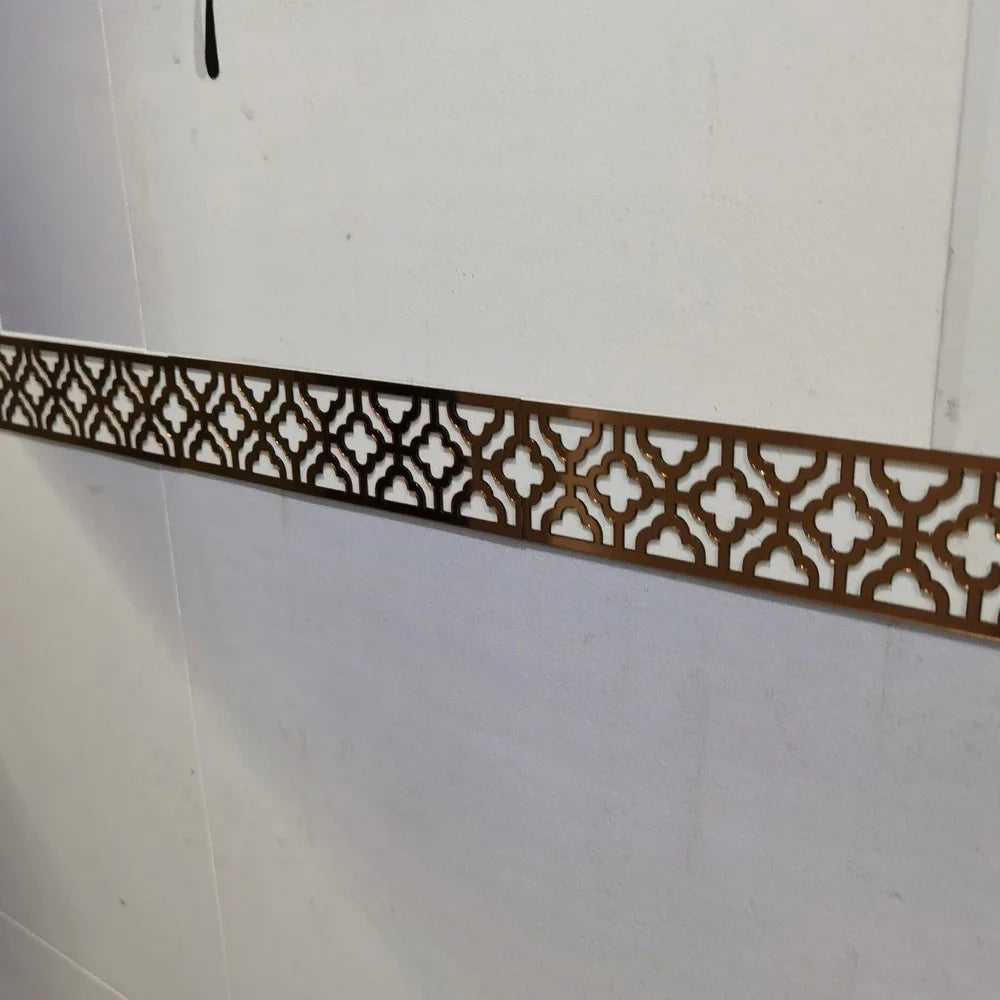 A decorative brown acrylic mirror border with an intricate geometric pattern mounted on a white wall.