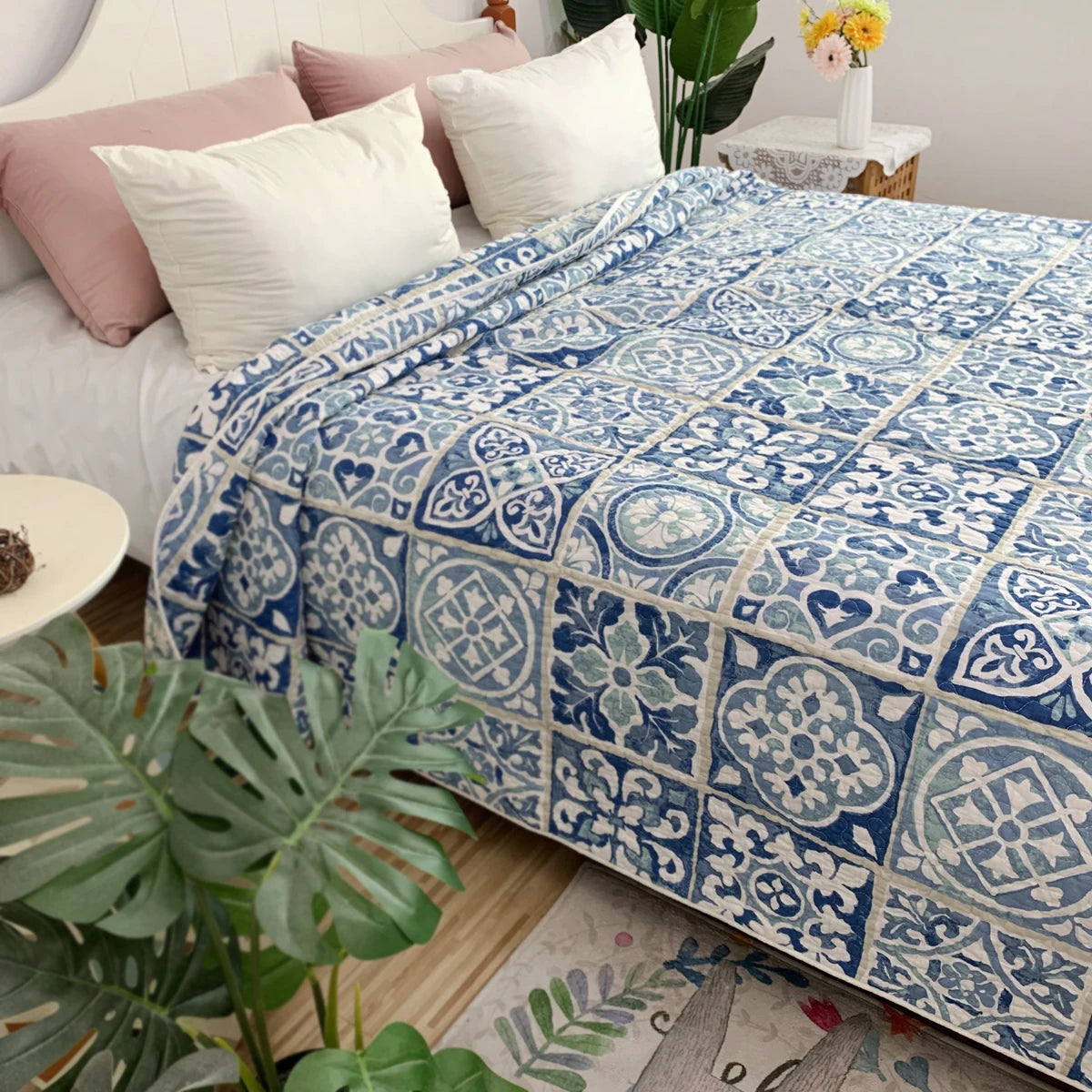 A blue and white patterned cotton bedspread is displayed on a bed with pink pillows and green plants.