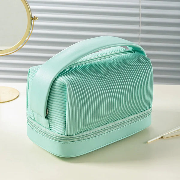 Una bolsa de maquillaje de cuero sintético estilo acordeón verde menta sobre una superficie blanca junto a un espejo circular