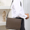 A person wearing a white shirt and black pants holds a brown patterned crossbody bag.