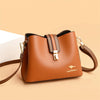 A brown leather shoulder bag with a gold clasp and brown strap resting on a light background.
