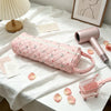 A pink quilted cotton hair dryer storage bag with a handle resting on a white surface next to a pink comb.