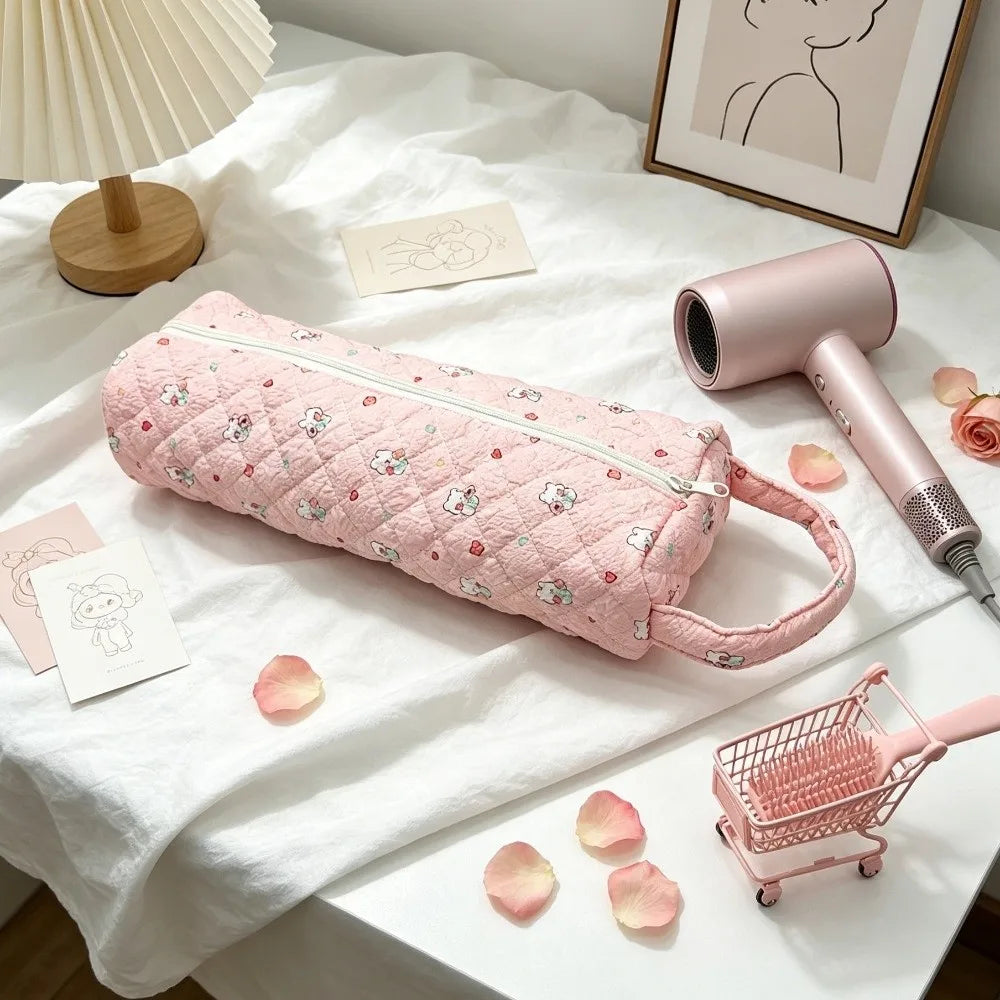 A pink quilted cotton hair dryer storage bag with a handle resting on a white surface next to a pink comb.