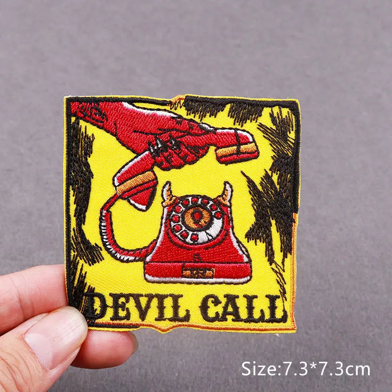 A hand holds an embroidered patch featuring a red hand grasping a red iron and a red skull design on a yellow background.