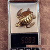 A brass or copper figurine of a turtle is displayed on a rectangular metal plate.
