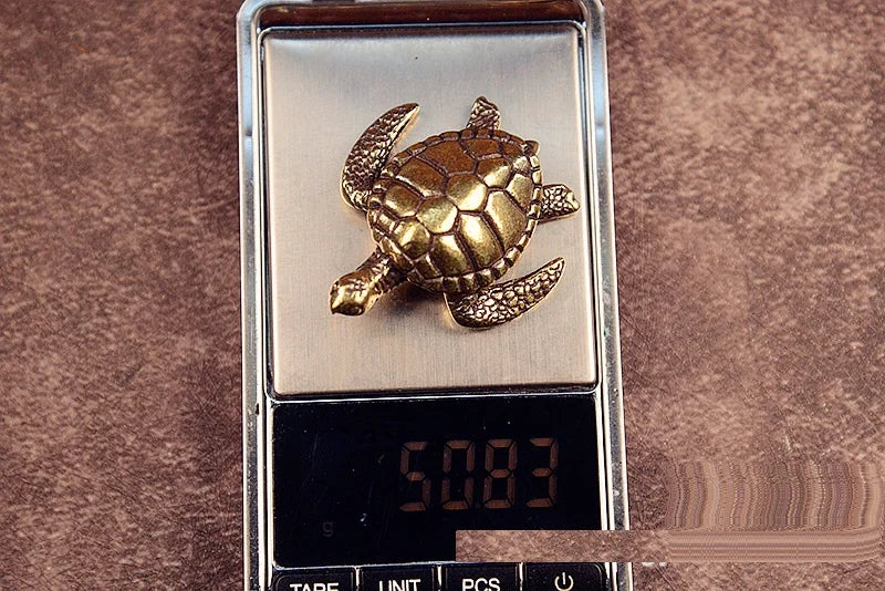 A brass or copper figurine of a turtle is displayed on a rectangular metal plate.
