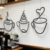 A set of three black iron art coffee cup wall decor pieces hanging on a white wall above a coffee machine.