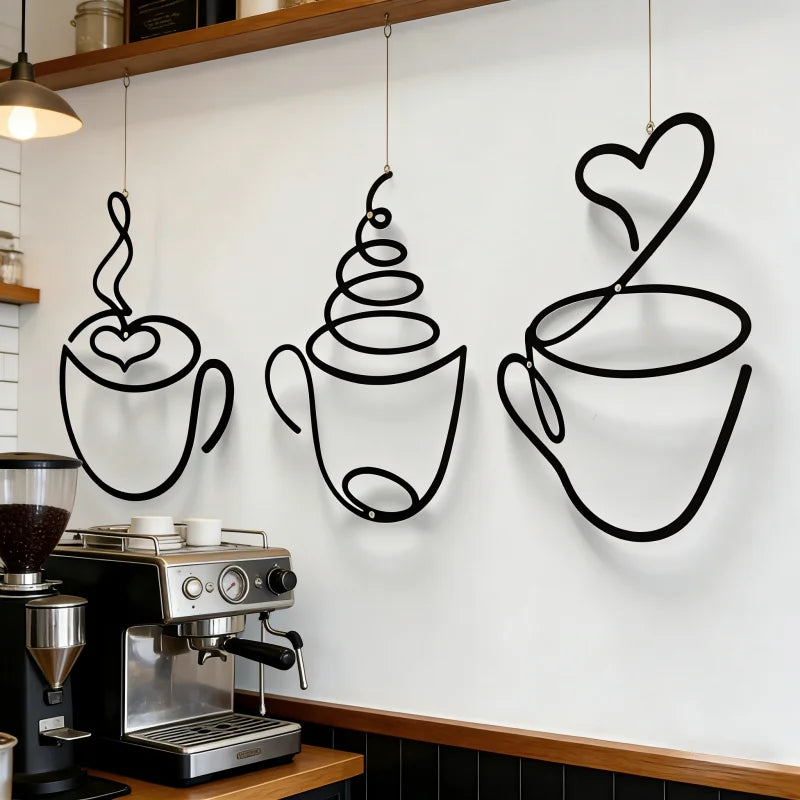 A set of three black iron art coffee cup wall decor pieces hanging on a white wall above a coffee machine.
