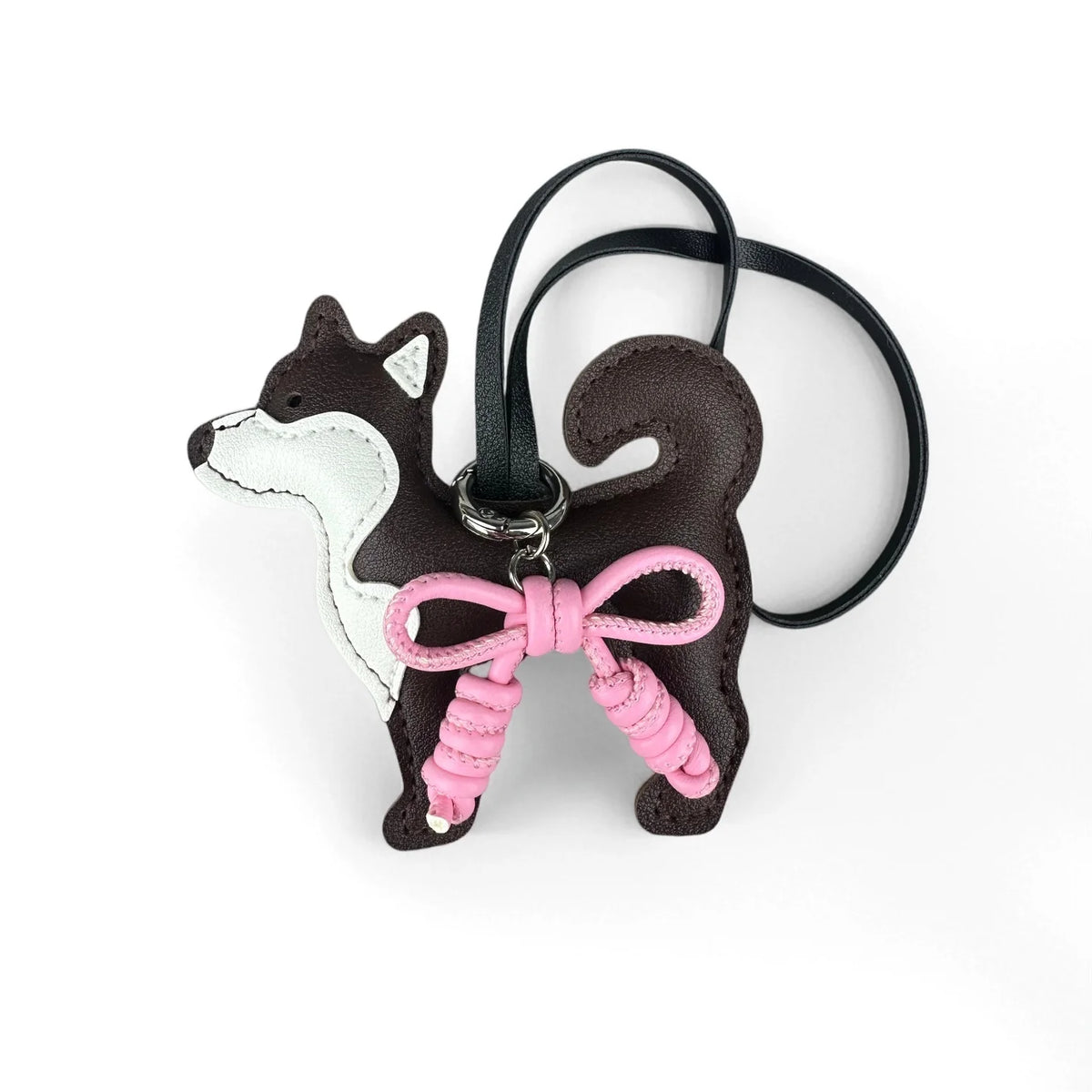 A dark brown and white Shiba Inu PU leather bag charm with a pink braided bow on a black strap.